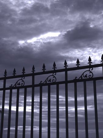 Gloomy Sky and Iron Gate -- a darkening sky with a wrought iron fence seen in silhouetteの写真素材