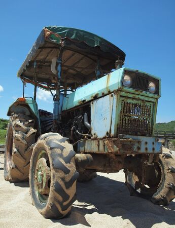 A vintage tractor sits on a sand beach against a blue skyの写真素材
