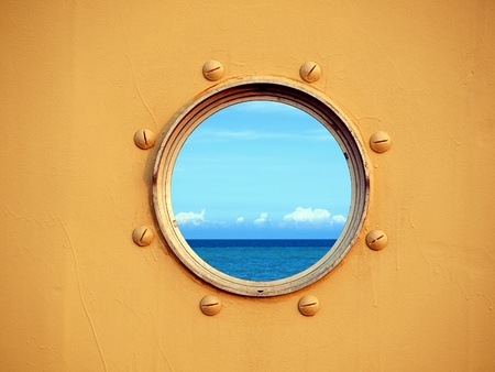 Looking through a porthole of a ship one can see the blue ocean and sky.の写真素材