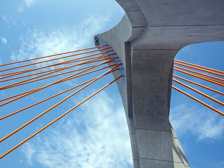 The single tower of a cable stayed bridge with orange steel cables
