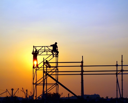 Construction workers high up on a scaffold seen against the setting sunの写真素材