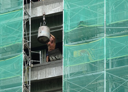 KAOHSIUNG, TAIWAN -- JULY 4, 2014: An elderly  worker at a construction site unloads a bucket of...