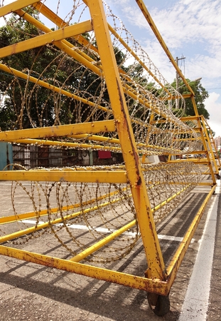 A yellow painted metal barrier with razor wire is used to guard a military installationのeditorial素材