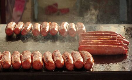 An outdoor vendor roasts fresh pork sausages on a grillの写真素材