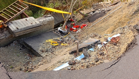 A road and built structures are damaged by a landslide