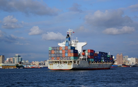 KAOHSIUNG, TAIWAN -- AUGUST 13 , 2017: A fully loaded large container ship enters Kaohsiung port. In the back one can see the skyline of the city.のeditorial素材