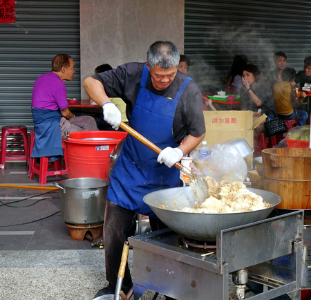 KAOHSIUNG, TAIWAN -- FEBRUARY 17, 2018: A man at an outdoor food stall cooks fried rice in a large wok.のeditorial素材