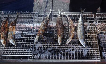 A street vendor cooks Pacific saury on a charcoal grill
