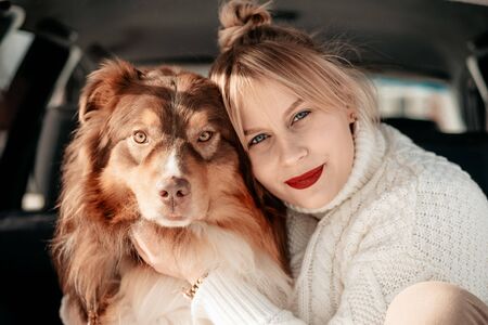 Beautiful woman sit and cuddle in the trunk of a minivan with a dog breed Lassie Australian...