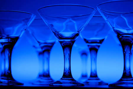 Wineglasses arranged in rows on the table in blue lightの写真素材