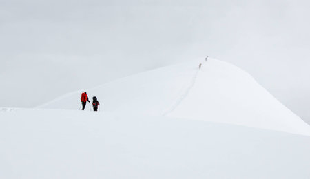 Mountaineers going down the snow trail on the high altitude mountain ridge in fog