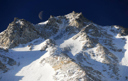 High mountain view  with glacial slope of mountain peak and the Moon on the sky