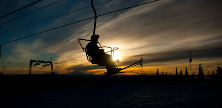 Silhouette of lonesome skier climbing up by the chair lift in sunriseの写真素材