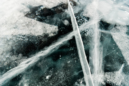 Cracked black ice of frozen lake. Nature abstract background.の写真素材