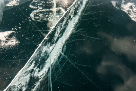 Cracked black ice of frozen lake. Nature abstract background.の写真素材