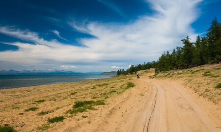 Bicycle tourist walking by the sandy road in dunes along the lake shore.の写真素材