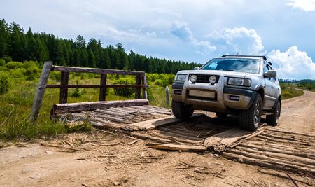 Off-road vehicle on the decayed small wooden bridge on the gravel bumpy road