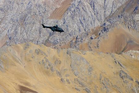 Military rescue helicopter flying over the mountain ridge.  Rocky mountain slope background.の写真素材