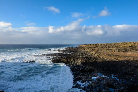 Black frozen lava of the volcano close up. Tenerife. beautiful blue sky with clouds and sea waves