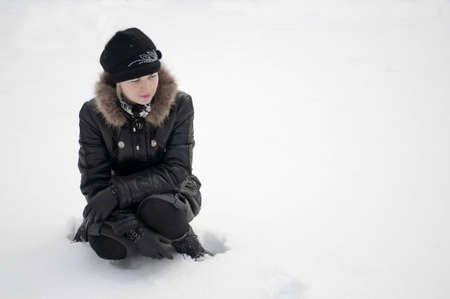 The girl in black clothes sits in white snowの写真素材