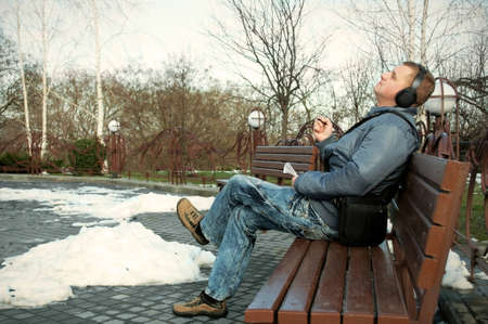 The guy sits on a bench and listens to musicの写真素材