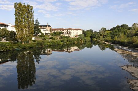 Sky reflection on a river with trees and some little buildingsの写真素材