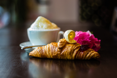 Croissant with butter and marmalade with cup of cappuccino on wooden table in cafeの写真素材