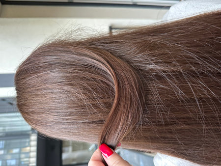 A hand is twisting a section of long, shiny brown hair, demonstrating hair styling techniques and emphasizing the beauty and health of hair in a contemporary environmentの写真素材