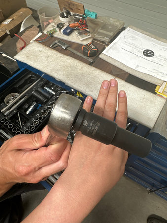 Mechanic is adjusting a tool with a wrench in a workshop, surrounded by various equipment and tools, highlighting skilled craftsmanship and focused workの写真素材