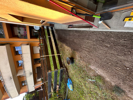 Outdoor garden pathway under construction with freshly turned soil, wooden fence, and gardening tools, highlighting landscaping and home improvement activitiesの写真素材