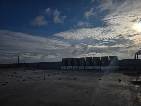 Industrial air conditioning units are positioned on a rooftop, with a vast sky filled with clouds,...