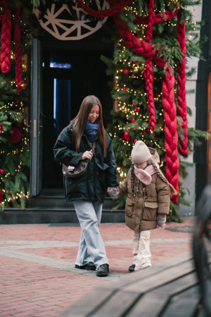Lwiw, Ukraine - November 28, 2025: Asian mother and daughter stroll together, surrounded by vibrant holiday decorations, creating a joyful winter atmosphereのeditorial素材