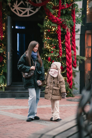 Lwiw, Ukraine - November 28, 2025: Mother and daughter stroll together in a beautifully decorated street, surrounded by festive lights and greeneryのeditorial素材