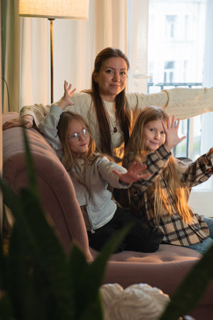 Mother and two daughters are playfully posing on a comfortable sofa in a bright living room, showcasing their bond and joyful family momentsの写真素材