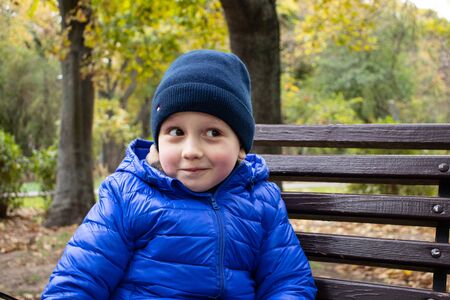 Portrait of a smiling boy who sits on a park bench in autumnの写真素材