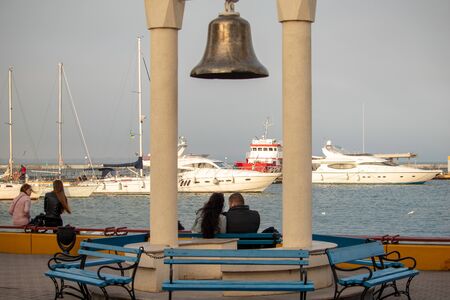 A man and a woman sit under a bell on a bench in the port and look at the sea and yachts - Ukraine, Odessa, 09,11,2019のeditorial素材