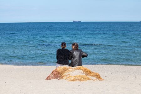 Two girls sit on a rock by the seaの写真素材