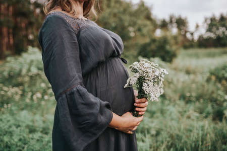 Close-up of pregnant woman with hands on her belly on nature backgroundの写真素材