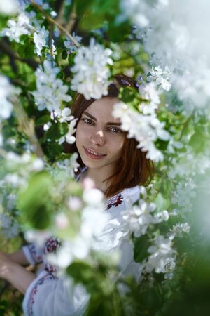 beautiful young brunette woman standing near the apple tree on a warm summer dayの写真素材