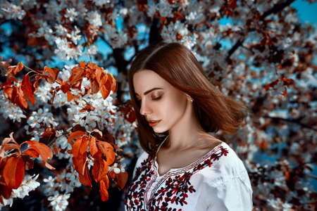 beautiful young brunette woman standing near the tree with red leafs on a warm summer dayの写真素材