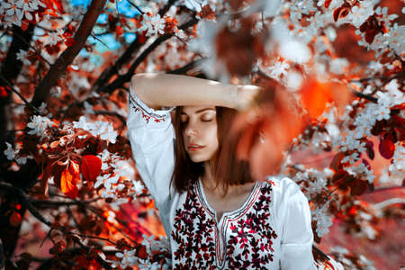 beautiful young brunette woman standing near the tree with red leaves on a warm summer dayの写真素材