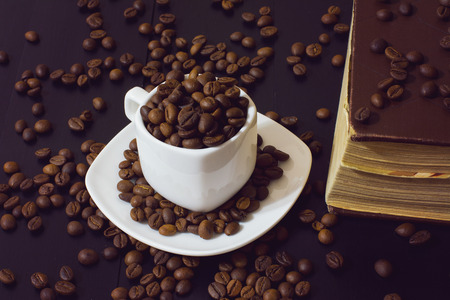 small white cup with coffee beans and old book on a dark wooden backgroundの写真素材