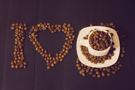 small white cup with coffee beans on a dark wooden background. I love coffee compositionの写真素材