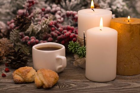 Cup of coffee, candle, cookies, fir branch in snow on wooden backgroundの写真素材