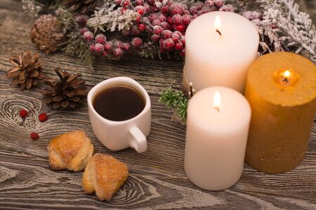 Cup of coffee, candle, cookies, fir branch in snow on wooden backgroundの写真素材