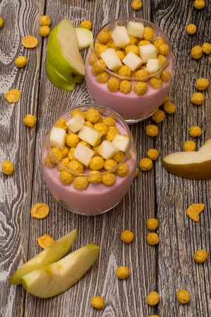 Yogurt desserts with muesli and slices of apple on wooden backgroundの写真素材