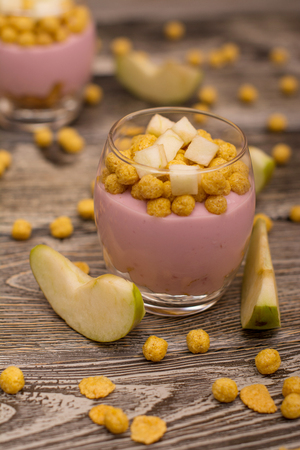 Yogurt desserts with muesli and slices of apple on wooden backgroundの写真素材