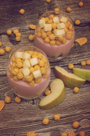 Yogurt desserts with muesli and slices of apple on wooden backgroundの写真素材