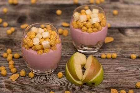 Yogurt desserts with muesli and slices of apple on wooden background