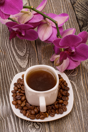 Small white cup of coffee, roasted coffee beans, orchid on wooden backgroundの写真素材